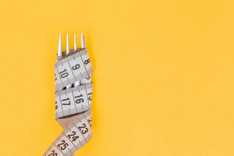 Eine mit einem Maßband umwickelte Gabel symbolisiert die Kausalität zwischen Ernährung und Bauchumfang